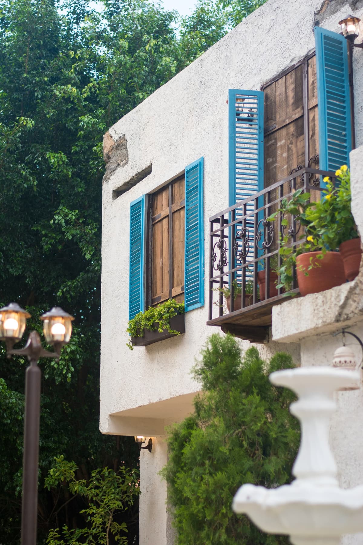 Fachada con balc&oacute;n de persianas azules, faroles y fuente en Bella Nonna