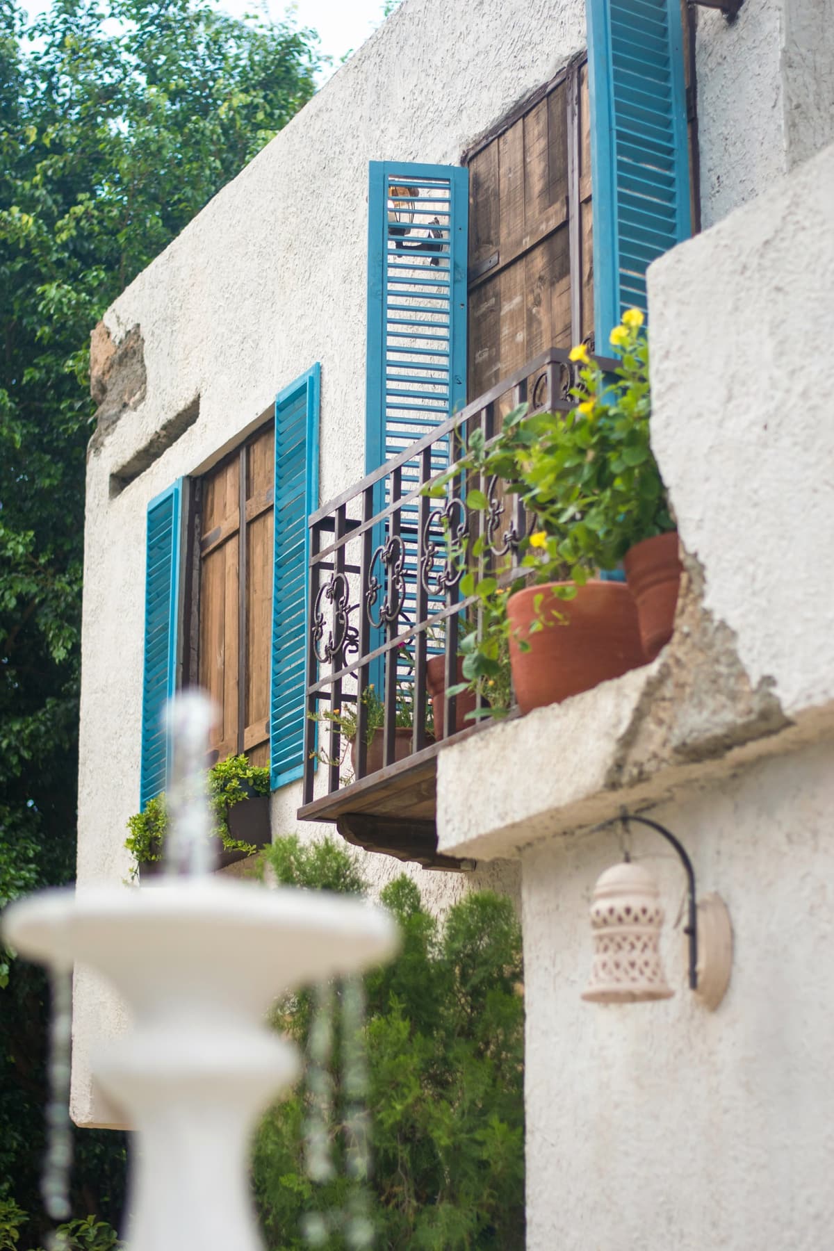 Fachada blanca con balcón de persianas azules y fuente en Bella Nonna
