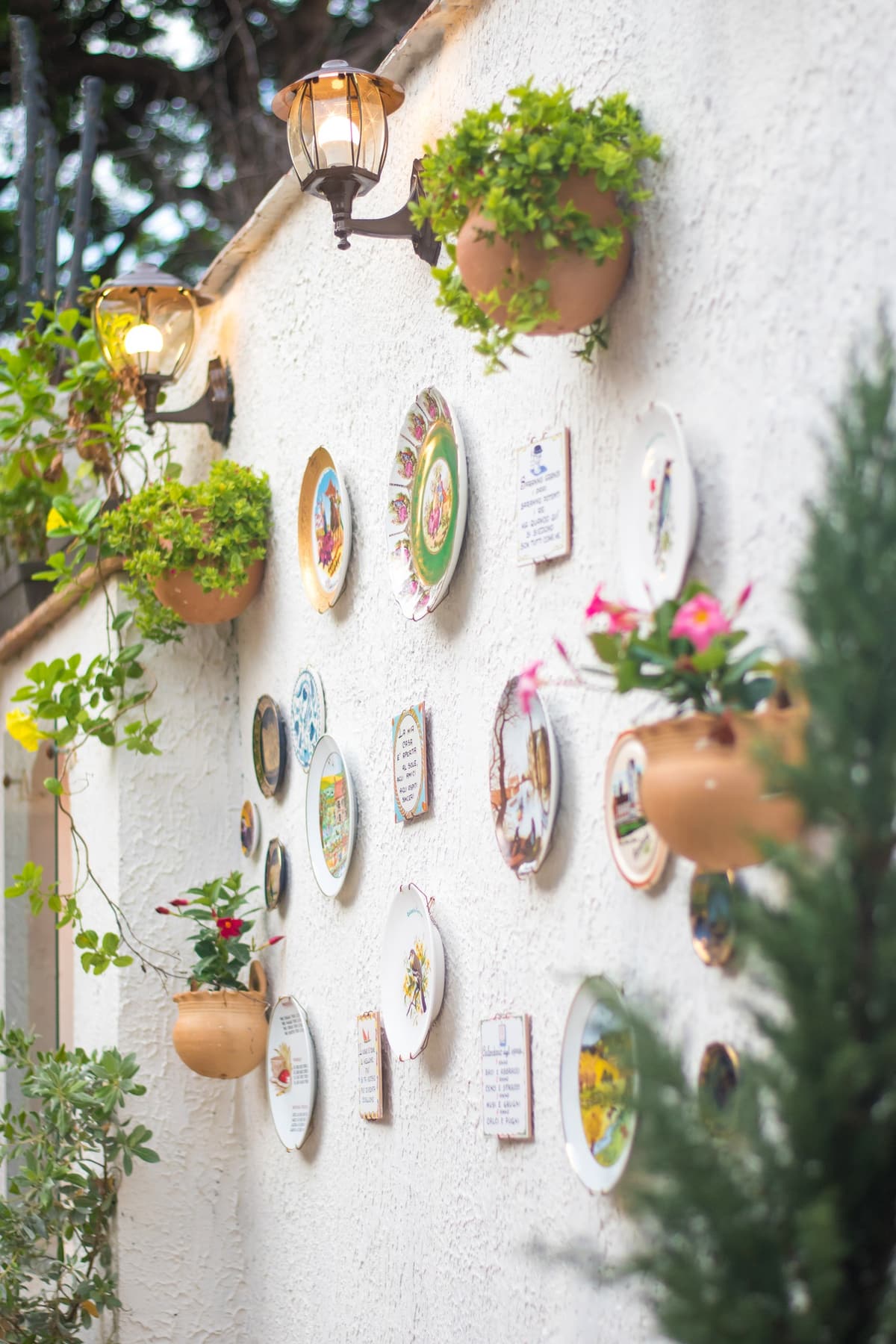 Pared blanca decorada con platos de cer&aacute;mica, faroles y macetas